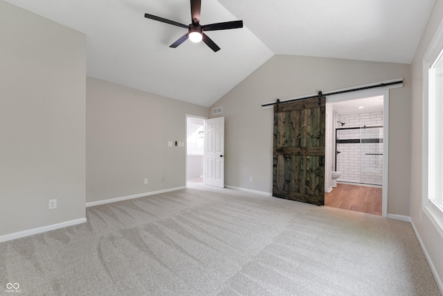 unfurnished bedroom with carpet flooring, lofted ceiling, a barn door, ensuite bathroom, and baseboards