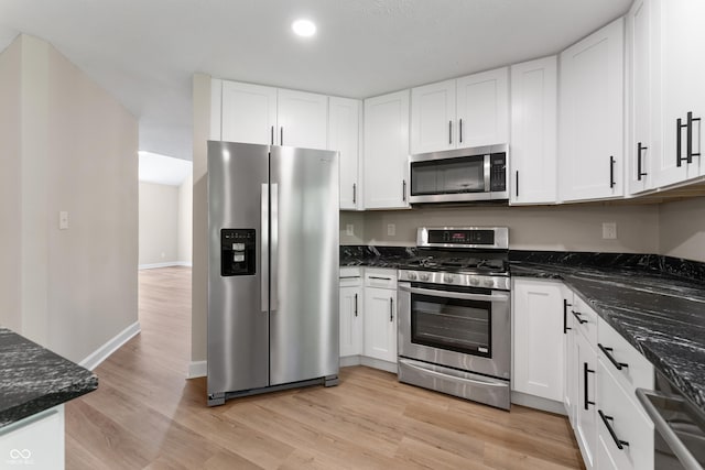 kitchen with appliances with stainless steel finishes, white cabinets, light wood-style flooring, dark stone counters, and recessed lighting