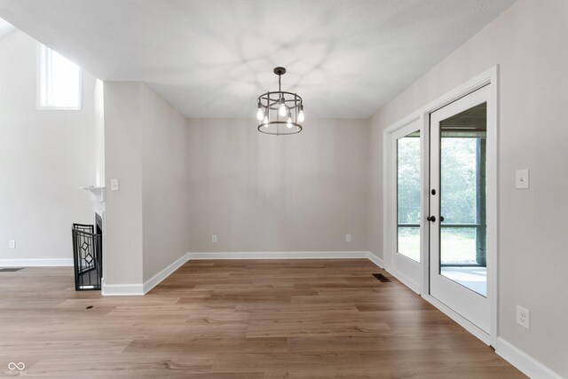 unfurnished dining area with wood finished floors, a chandelier, baseboards, a fireplace, and french doors