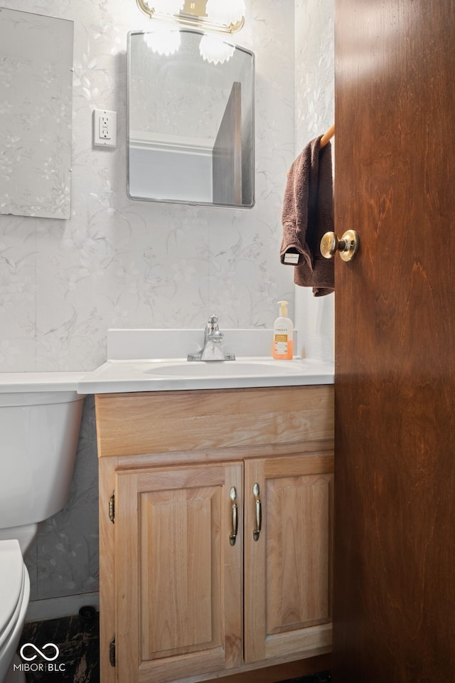 half bath featuring vanity, toilet, and wallpapered walls