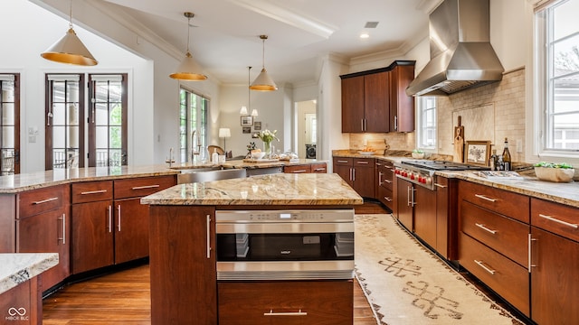 kitchen with ornamental molding, wall chimney range hood, a center island, and wood finished floors