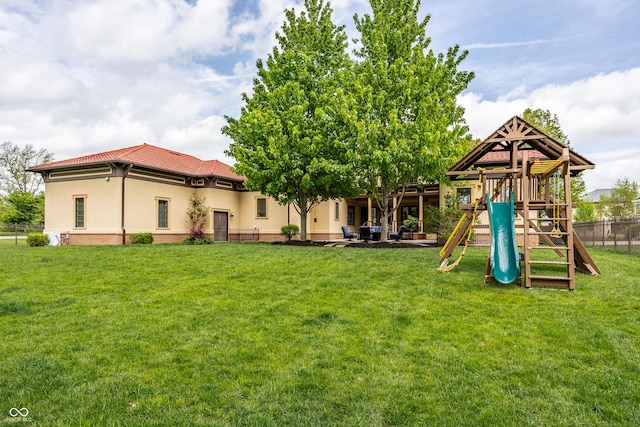 back of house featuring a lawn, fence, stucco siding, a tile roof, and a playground