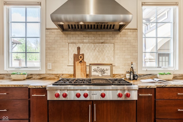 kitchen featuring light stone countertops, stainless steel gas stovetop, wall chimney exhaust hood, and tasteful backsplash