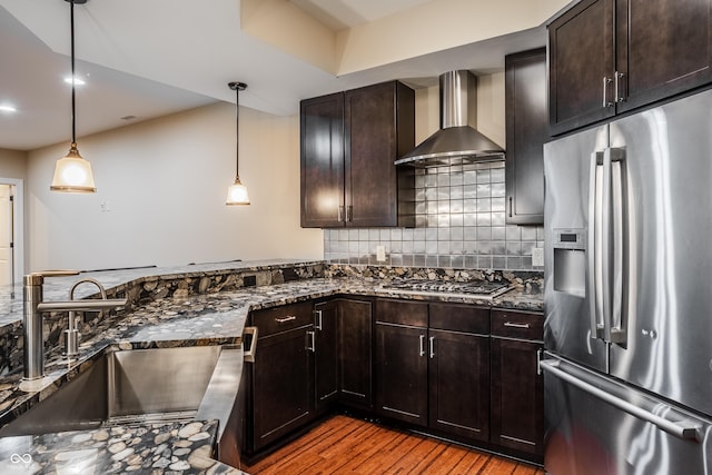 kitchen featuring a sink, wall chimney range hood, dark stone counters, backsplash, and appliances with stainless steel finishes