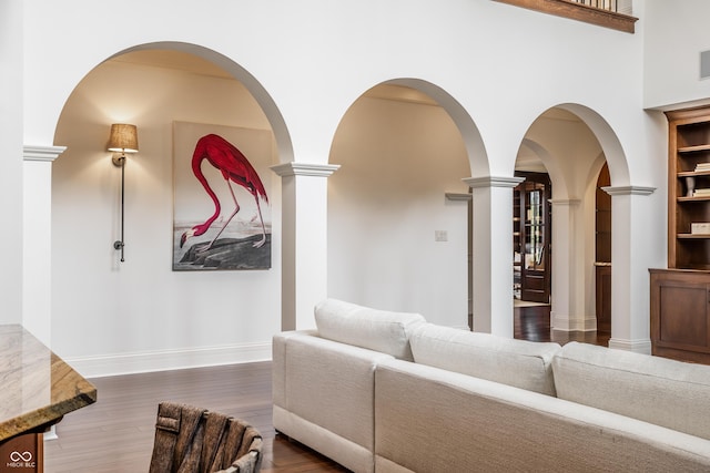 living area with baseboards, dark wood-type flooring, and decorative columns