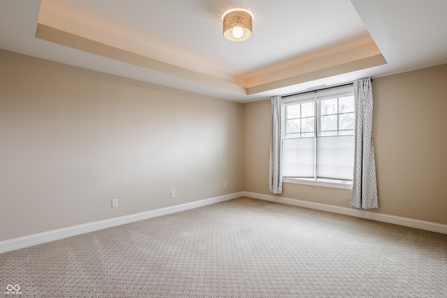 carpeted spare room featuring a tray ceiling and baseboards