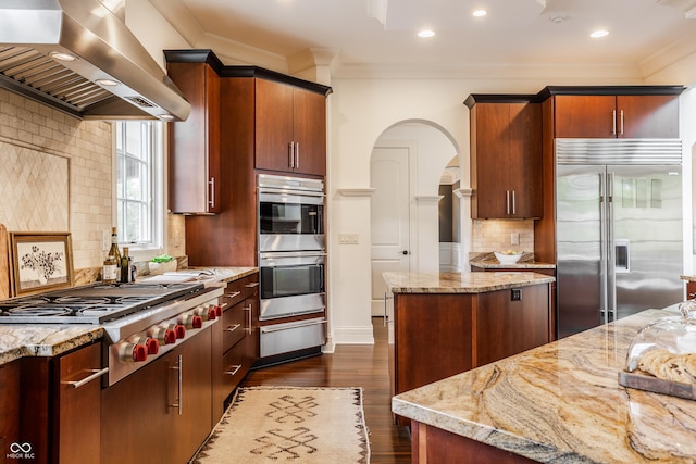 kitchen featuring stainless steel appliances, wall chimney range hood, ornamental molding, a warming drawer, and arched walkways
