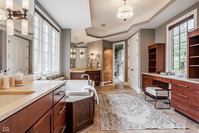 full bath with a tray ceiling, two vanities, a tub, and a healthy amount of sunlight