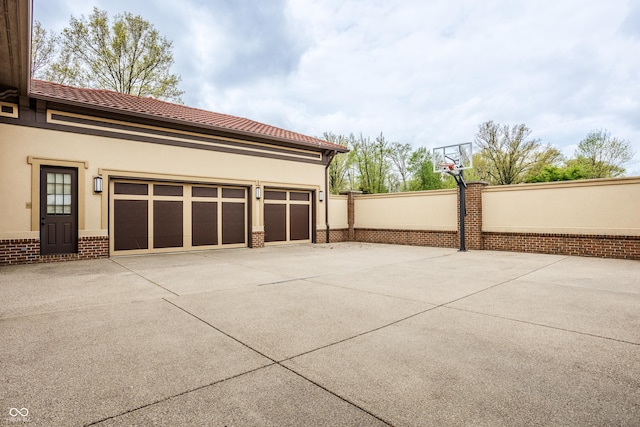 garage featuring concrete driveway, basketball hoop, and fence