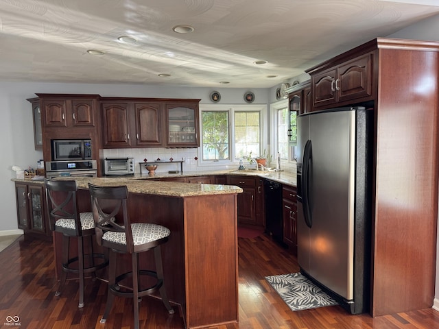 kitchen featuring stainless steel appliances, a kitchen breakfast bar, light stone counters, dark wood-style flooring, and a kitchen island