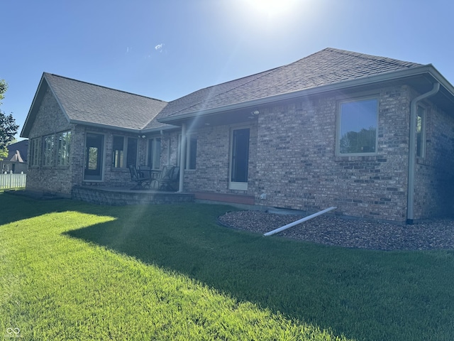 back of property featuring brick siding, a yard, and roof with shingles