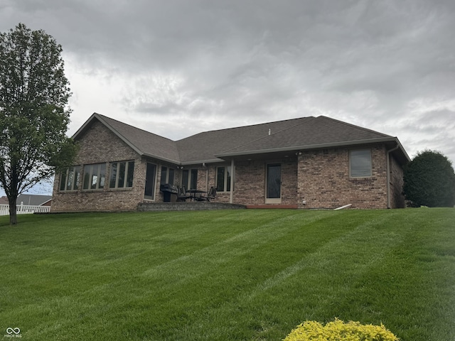 back of house featuring brick siding, a yard, and roof with shingles