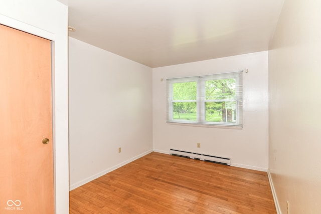 spare room featuring a baseboard heating unit, light wood-style flooring, and baseboards