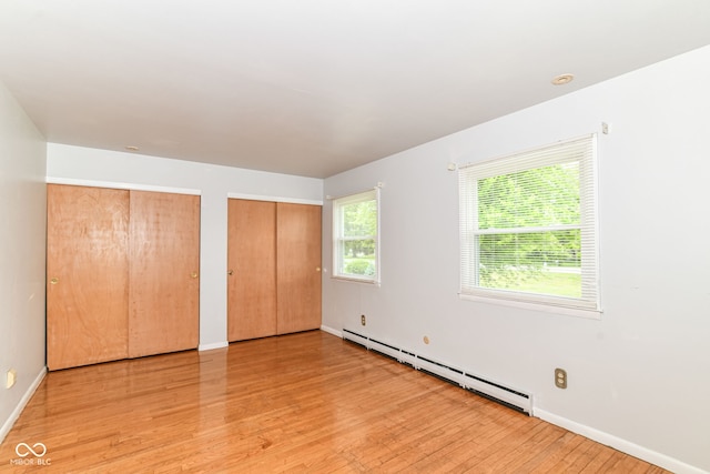 unfurnished bedroom with baseboard heating, multiple closets, light wood-style flooring, and baseboards