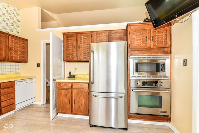 kitchen featuring appliances with stainless steel finishes, light countertops, backsplash, brown cabinets, and light wood-style flooring