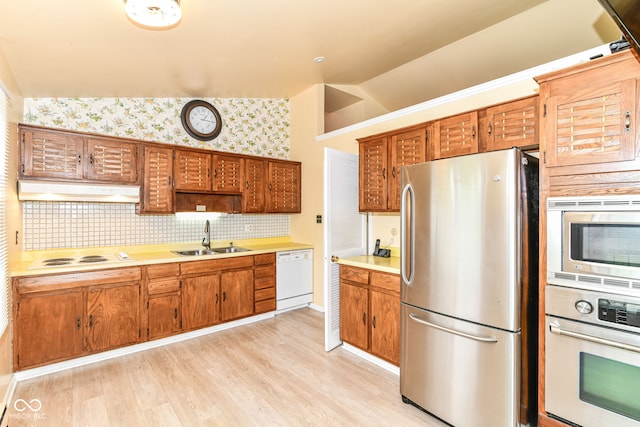 kitchen with stainless steel appliances, a sink, under cabinet range hood, vaulted ceiling, and light countertops