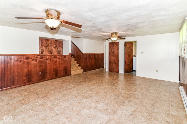 unfurnished living room with ceiling fan, a wainscoted wall, wood walls, stairs, and tile patterned floors