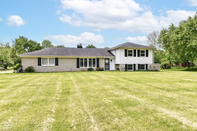 split level home featuring brick siding, a front yard, and a chimney