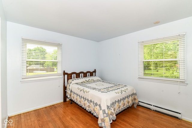 bedroom featuring baseboard heating, multiple windows, wood finished floors, and baseboards