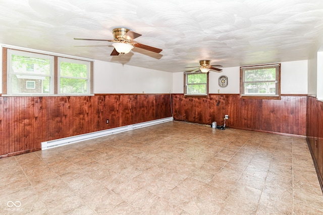 empty room featuring wainscoting, a ceiling fan, wood walls, and light floors