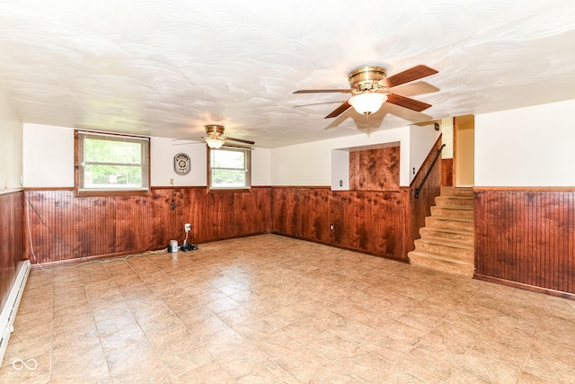unfurnished room featuring wainscoting, ceiling fan, wooden walls, baseboard heating, and stairs