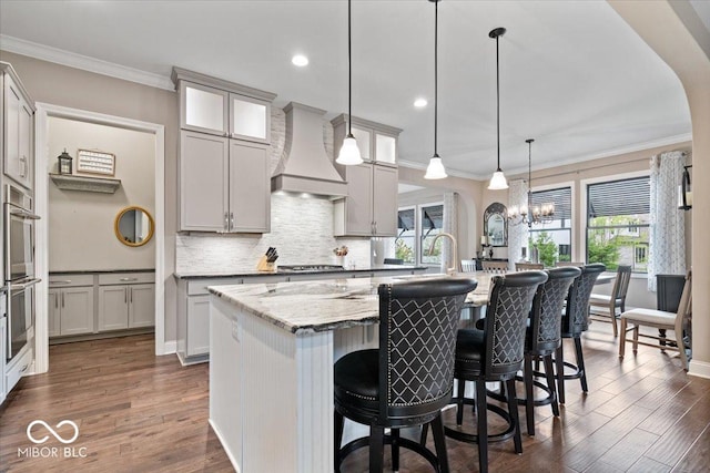 1013 Domino Dr, Carmel, IN 46032 - kitchen featuring ornamental molding, a kitchen island with sink, custom exhaust hood, and dark wood finished floors