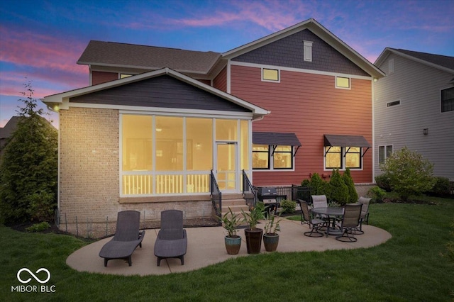 1013 Domino Dr, Carmel, IN 46032 - back of house at dusk featuring brick siding, a sunroom, a patio area, entry steps, and a lawn