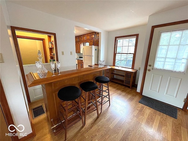 interior space featuring brown cabinets, light wood finished floors, freestanding refrigerator, a peninsula, and visible vents
