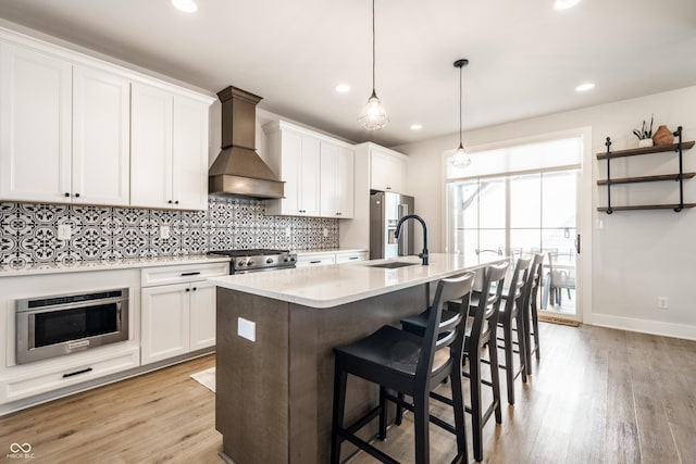 544 N Beville Ave, Indianapolis, IN 46201 - kitchen featuring custom exhaust hood, appliances with stainless steel finishes, decorative backsplash, an island with sink, and light wood-type flooring