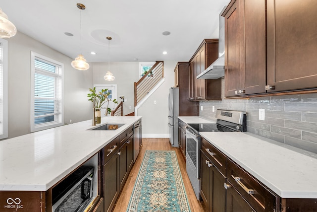 715 Terrace Ave, Indianapolis, IN 46203 - kitchen featuring stainless steel appliances, a kitchen island with sink, wall chimney range hood, light wood finished floors, and decorative backsplash