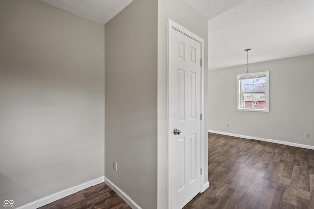 hallway featuring dark wood-type flooring, a textured ceiling, and baseboards