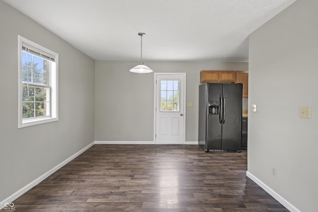 kitchen with hanging light fixtures, black refrigerator with ice dispenser, brown cabinetry, baseboards, and dark wood-style floors