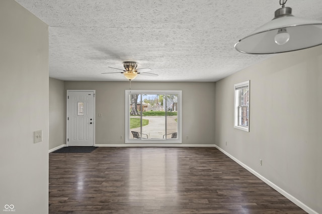unfurnished living room featuring baseboards, a textured ceiling, and dark wood finished floors
