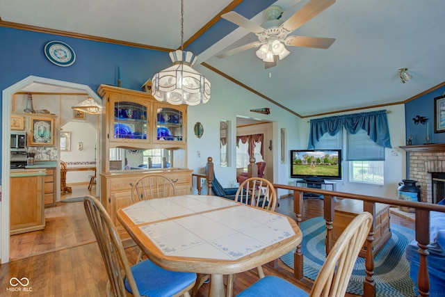 dining space with crown molding, lofted ceiling with beams, a brick fireplace, and light wood-style flooring