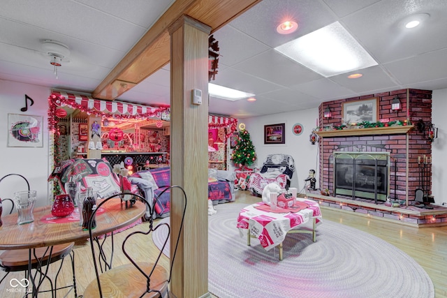 game room with a brick fireplace, recessed lighting, a paneled ceiling, and wood finished floors
