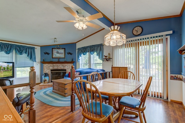 dining area with vaulted ceiling with beams, ceiling fan with notable chandelier, wood finished floors, and a brick fireplace