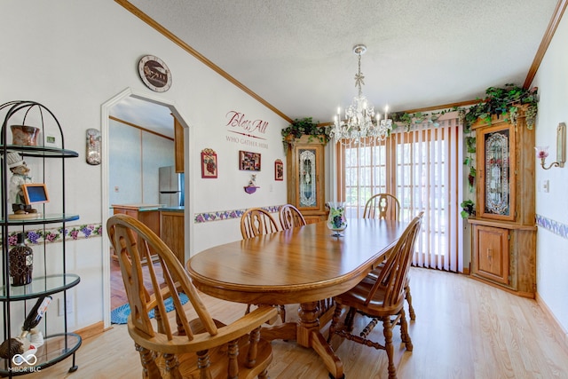 dining area with crown molding, a textured ceiling, an inviting chandelier, and light wood-style flooring