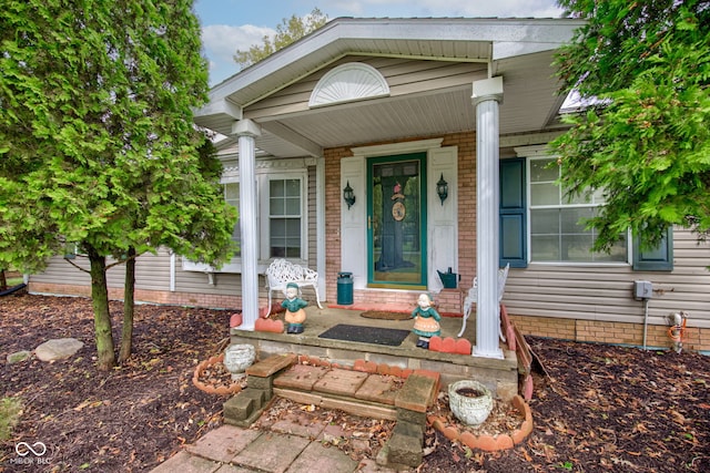 doorway to property with a porch and brick siding