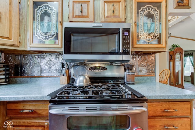 kitchen featuring glass insert cabinets, appliances with stainless steel finishes, backsplash, and light countertops