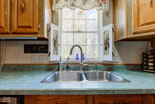 kitchen with brown cabinetry, a sink, and wallpapered walls