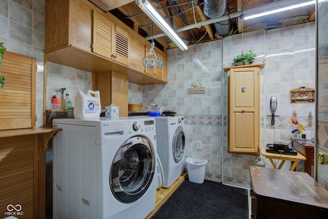 clothes washing area featuring cabinet space, washing machine and dryer, and tile walls