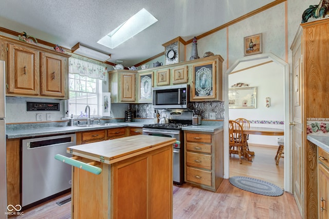 kitchen featuring vaulted ceiling with skylight, appliances with stainless steel finishes, a center island, light wood-type flooring, and a sink
