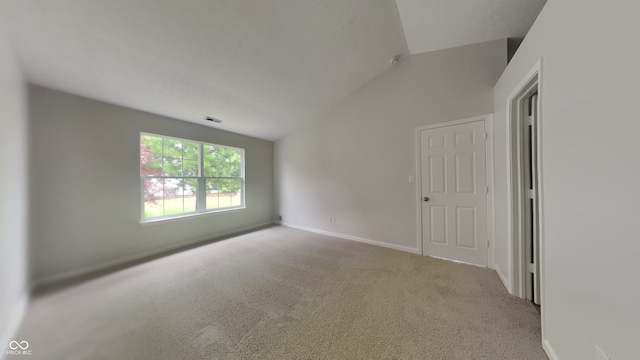 carpeted empty room with baseboards, visible vents, and lofted ceiling