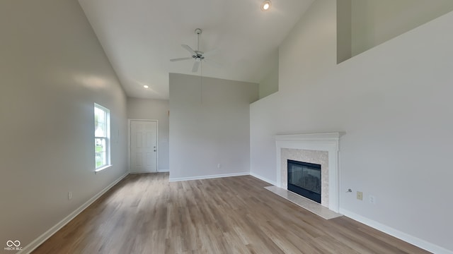 unfurnished living room featuring a ceiling fan, a high end fireplace, wood finished floors, high vaulted ceiling, and baseboards