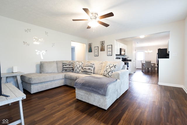 living room featuring dark wood-style flooring, ceiling fan with notable chandelier, and baseboards