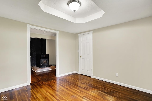 spare room with wood finished floors, baseboards, and a wood stove
