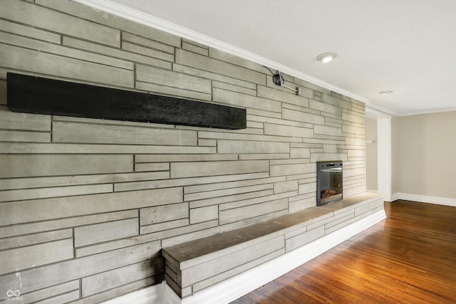 detailed view of ornamental molding, baseboards, a stone fireplace, and wood finished floors