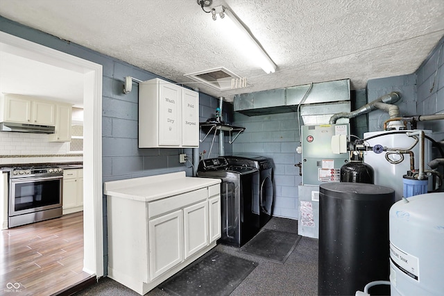kitchen featuring stainless steel range with gas stovetop, under cabinet range hood, washer and dryer, a textured ceiling, and concrete block wall