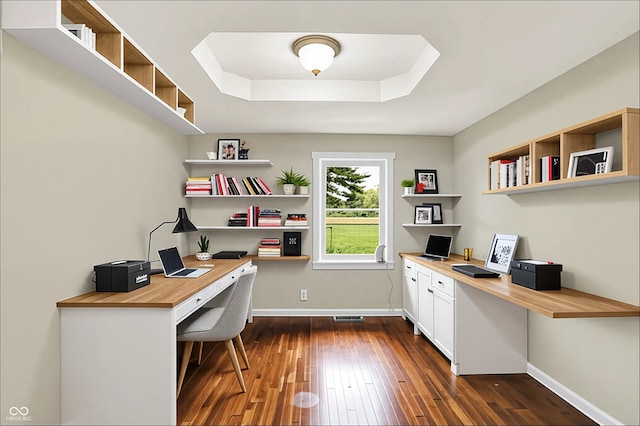 office area with built in study area, dark wood-style flooring, baseboards, and a tray ceiling