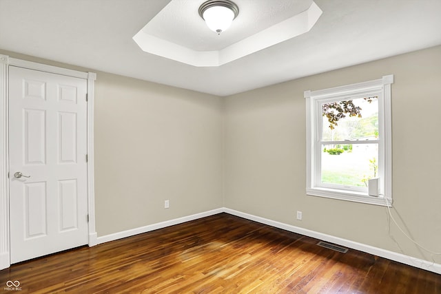 spare room featuring hardwood / wood-style floors, baseboards, and a raised ceiling